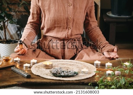 Woman meditating with palo santo in studio, cleaning space with smoke. Adult person using burning spiritual incenses at home