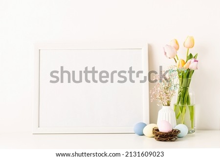 Home interior with easter decor. Mockup with a white frame spring tulips in vase, gypsophila and pastel colored eggs on light background