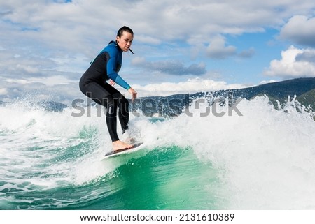 Young athletic female in wetsuit riding on endless waves behind a boat on sunny day. Woman practice wakeboarding, carving behind the baot. Watersport concept. Royalty-Free Stock Photo #2131610389