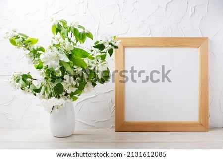 Wooden square picture frame mockup with tender apple blossom branches in the vase. Empty frame mock up for presentation design. Template framing for modern art.