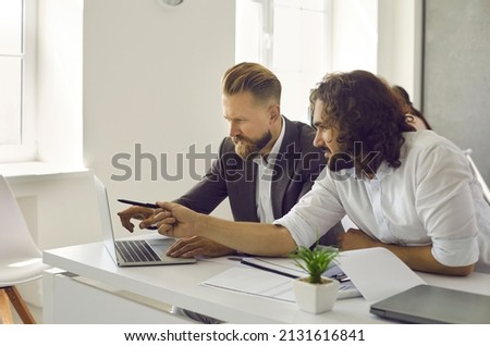 Two business people working together. Creative young businessmen, managers and coworkers sitting at office table, using laptop computer, analyzing marketing strategy, doing research, discussing ideas
