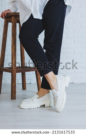 Legs of a young beautiful woman in black trousers and modern stylish white leather loafers. New collection of women's shoes spring-summer 2022 Royalty-Free Stock Photo #2131617533
