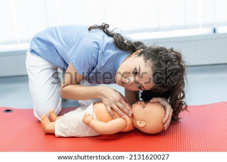CPR practitioner examining airway passages on infant dummy. Model dummy lays on table and two doctors practice first aid. Royalty-Free Stock Photo #2131620027