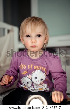 a smiling girl sitting on the bed in the children's room and looking at the camera, the morning of the child, the concept of children's goods.