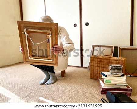 Elderly woman looking at a picture while decluttering in Japanese-style room Royalty-Free Stock Photo #2131631995