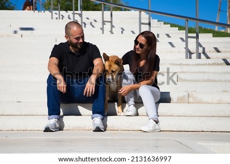 Adult couple sitting on a park bench with their dog posing for a family photo. One more in the family. Pets concept. 4 October World Pet Day.
