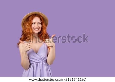 Atrractive caucasian redhead young woman wearing straw hat doing happy thumbs up gesture with hands and smiling posing on purple background and copy space.