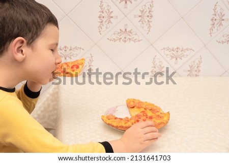 Child are eating homemade pizza with sausages, tomatoes and cheese sitting at the table in the kitchen close up with selective focus