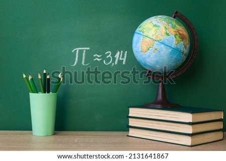 The Greek letter Pi is drawn in chalk on a green school blackboard with books, a globe, pencils in honor of the international day of March 14 Royalty-Free Stock Photo #2131641867
