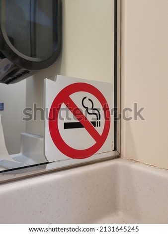 No Smoking red and white sign on public bathroom mirror 