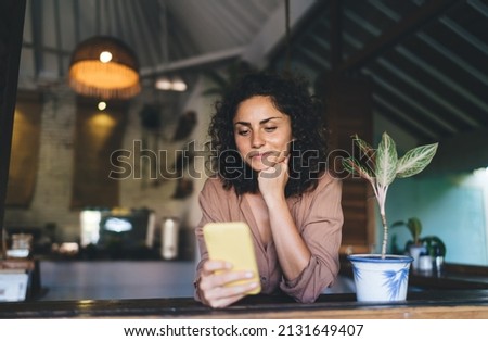 Pretty female blogger with smartphone enjoying leisure time for networking web pages, millennial woman checking email while messaging with friends in social media using 4g wireless connection Royalty-Free Stock Photo #2131649407