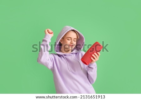 Woman in hoodie with wireless portable speaker enjoying music and dancing on green background Royalty-Free Stock Photo #2131651913