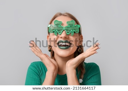 Happy young woman in eyeglasses on light background. St. Patrick's Day celebration