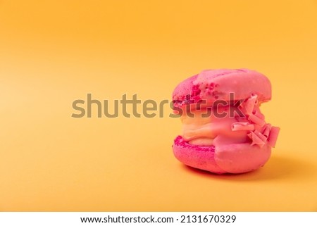 Delicious berry macaroons on a soft yellow-orange paper background. French meringue cookies macaron. Culinary and cooking concept. Copy space.