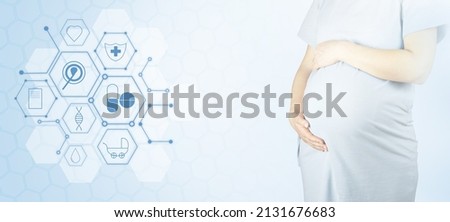 A burdensome woman keeps her hands on her stomach on a light background with copy space. The concept of pregnancy, motherhood, preparation and expectation. Copy space with medical symbols in honeycomb
