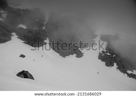 Two tinny skiers in the distance skiing down a slope into the fog