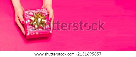 Women's hands holds a gift box on a pink background with space for text.