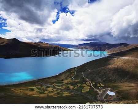 A scenic view of a lake surrounded by mountains in Tibet on cloudy sky background