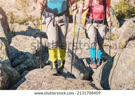 Two hikers wearing waterproof gaiters over trekking boots walking with hiking sticks among boulders in nature park. Clothing and equipment for backpacking and camping Royalty-Free Stock Photo #2131708409