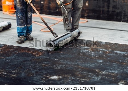 Construction workers, roofers installing rolls of bituminous waterproofing membrane for the waterproofing of new house. House waterproofing and insulation
 Royalty-Free Stock Photo #2131710781