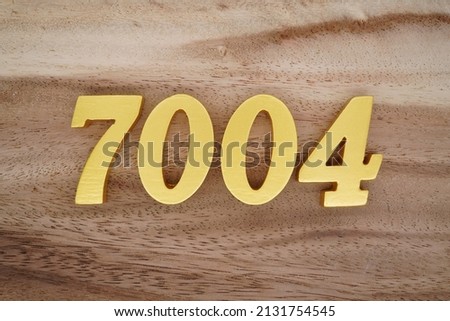 Wooden  numerals 7004 painted in gold on a dark brown and white patterned plank background.