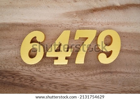 Wooden  numerals 6479 painted in gold on a dark brown and white patterned plank background.