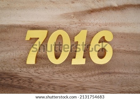 Wooden  numerals 7016 painted in gold on a dark brown and white patterned plank background.