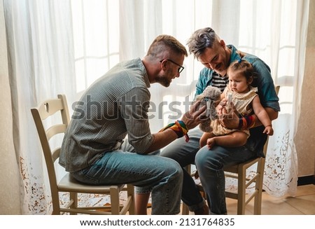 Male gay couple with adopted baby girl at home - Two handsome fathers playing with their daughter - Lgbtq+ family at home - Diversity concept and LGBTQ family relationship Royalty-Free Stock Photo #2131764835