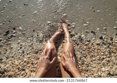 Woman legs and hands on beach first person picture, dipping toes in wet sand and sea shells close up, Sanibel Island Fort Myers Florida