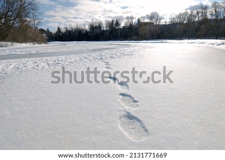 Footprints in loose snow in top of a frozen lake.