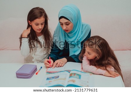 Young mother in hijab helping child daughter to doing homework. Happy Muslim family in home. Islam people education.	