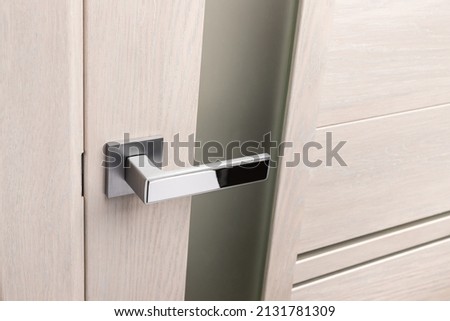 Close up of beautiful and stylish new metal door knob on modern interior door. Silver chrome handle on light beige door with frosted glass. Concept of interior details. Royalty-Free Stock Photo #2131781309