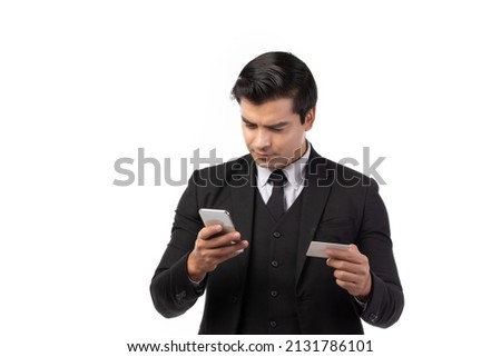 Handsome business man in black suit holding credit card and using smartphone for online shopping isolated on white background. Business, technology, ecommerce and online payment concept.