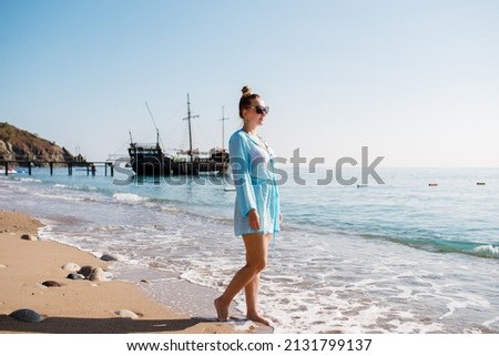 Blonde caucasian white woman in blue short dress walking and enjoying sunny day In Famara beach in the northwest of the island of Lanzarote,one of the most popular places to surf in the Canary Islands