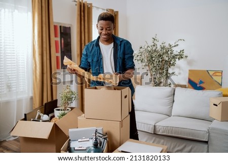 Unpacking cardboard boxes after moving, man cleans new apartment cluttered with things from previous home, looks at items, planning decorations, living room furnishings Royalty-Free Stock Photo #2131820133