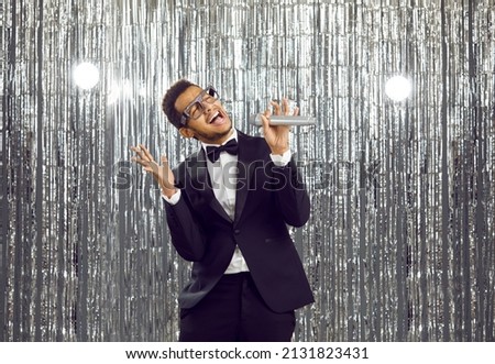 Overjoyed young African American man in formal suit sing in microphone have fun in nightclub. Smiling black guy relax rest enjoy karaoke in disco club. Entertainment and hobby concept. Royalty-Free Stock Photo #2131823431