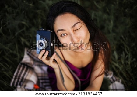 Beautiful asian woman with camera on grassland in garden vintage and retro tone, focus at the eye, shallow depth of field, soft focus, selective focus 