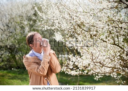 Woman allergic suffering from seasonal allergy at spring, posing in blossoming garden at springtime. Young woman sneezing in front of blooming tree. Spring allergy concept Royalty-Free Stock Photo #2131839917