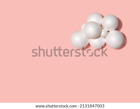 Foam balls forming a cloud against pastel pink background. Minimal creative layout.