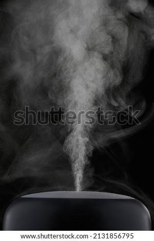 Modern air humidifier on black background. White steam close-up. The concept of humidification of the air. Royalty-Free Stock Photo #2131856795