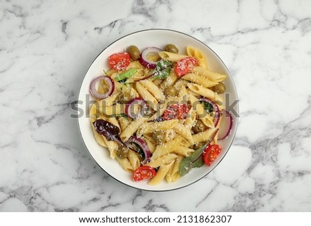 Bowl of delicious pasta with tomatoes, olives and onion on white marble table, top view