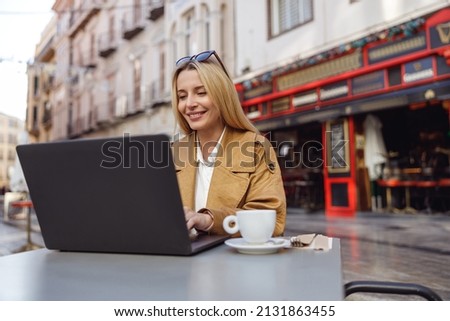 Happy female working on laptop while sitting at table in street cafe