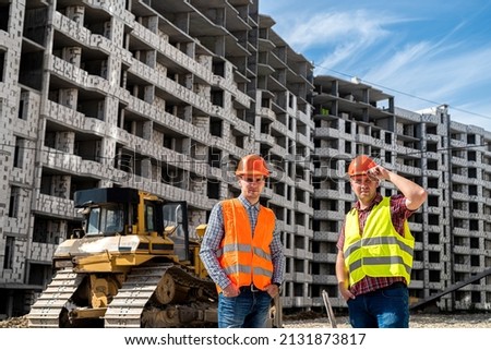 two strong young workers in uniform stand on the background of a new building. The concept of a new building