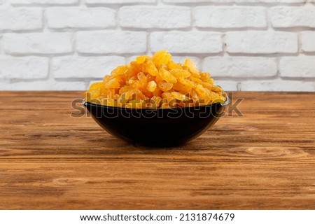 Raisins in a dark plate, on a wooden table against a brick wall.