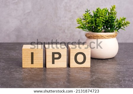 IPO concept. the IPO word is written on wooden cubes on a gray background. close-up of wooden elements. In the background is a green flower. IPO - short for Initial Public Offering