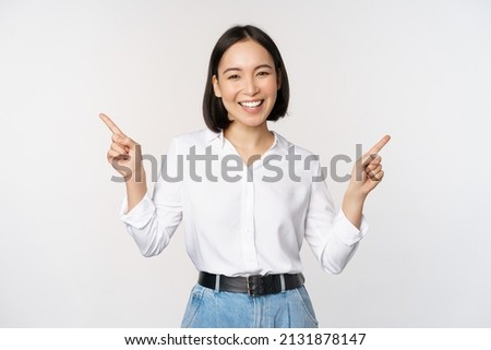 Image of beautiful asian woman pointing fingers left and right, making decision, showing two variants choices, standing over white background Royalty-Free Stock Photo #2131878147