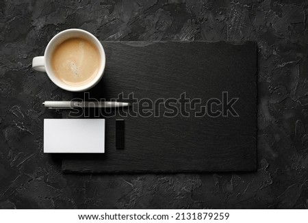 Blank business card, coffee cup, pen, usb flash drive and slate plate on black stone background. Template for placing your design. Flat lay.