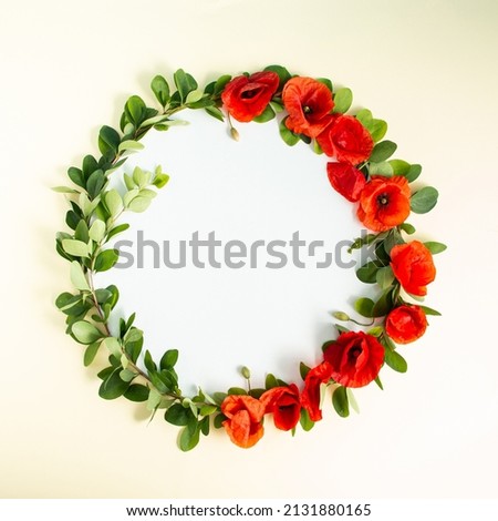 Round frame wreath with red poppies bloom and branches on sandy background. Minimal floral composition. Flat lay. Copy space.