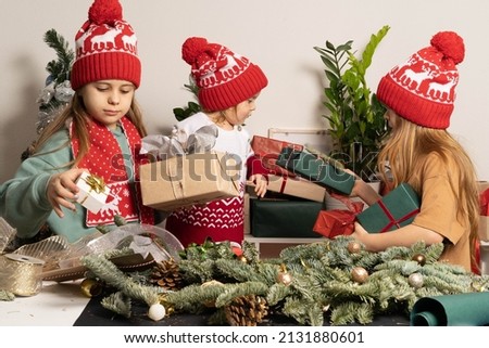 Three children in red Christmas hats are packing gifts and making Christmas decorations. The concept of hobby, family , holidays and holidays and eco-friendly lifestyle.