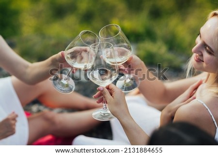 Cropped picture of three girls, sitting at nature, having picnic in a city park during summer holidays. Women clinking glasses of wine at a picnic.